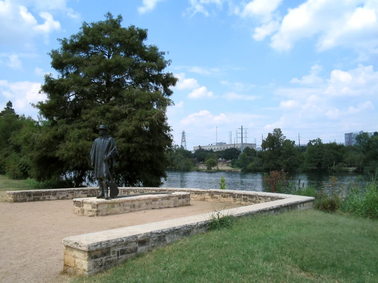 a statue sitting in a park next to a lake