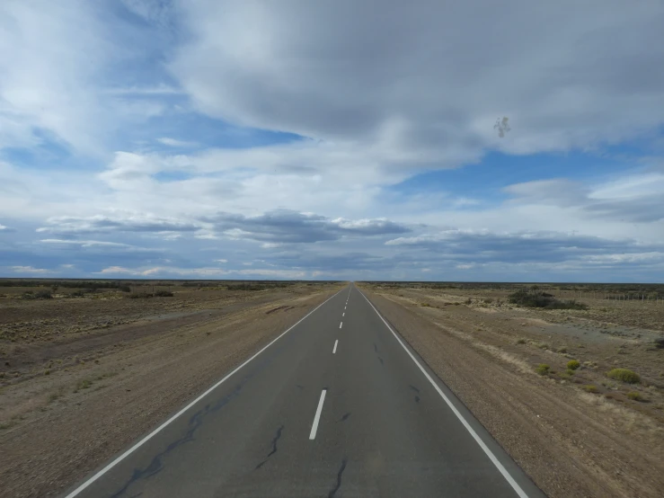 the vastly wide open highway is lined with dry bushes