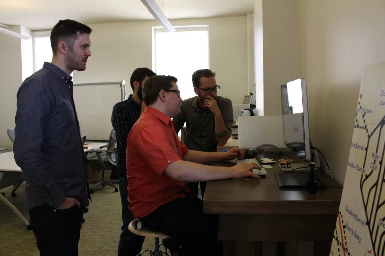 four men sit in front of a computer screen