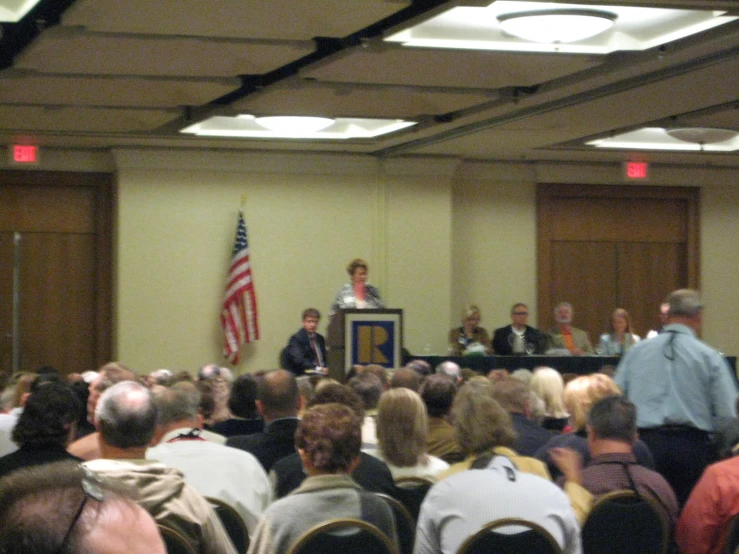 a crowd in a room looking on at a man giving a speech