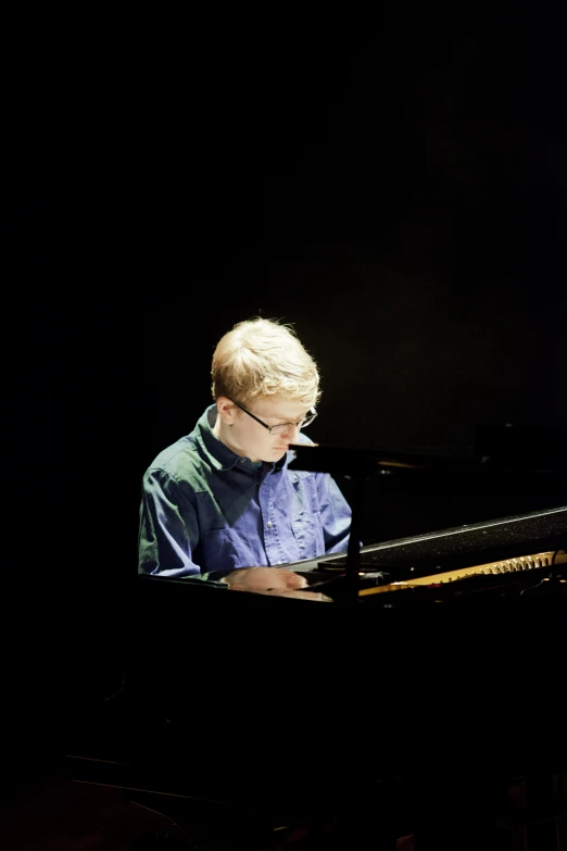 a man with blond hair and glasses sitting at a piano