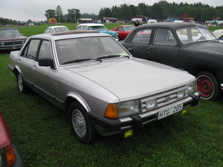 some older cars are parked on grass and other vehicles are in the background