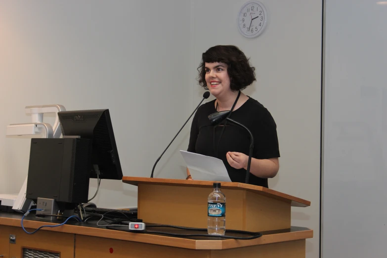 a woman is giving a speech in front of a monitor