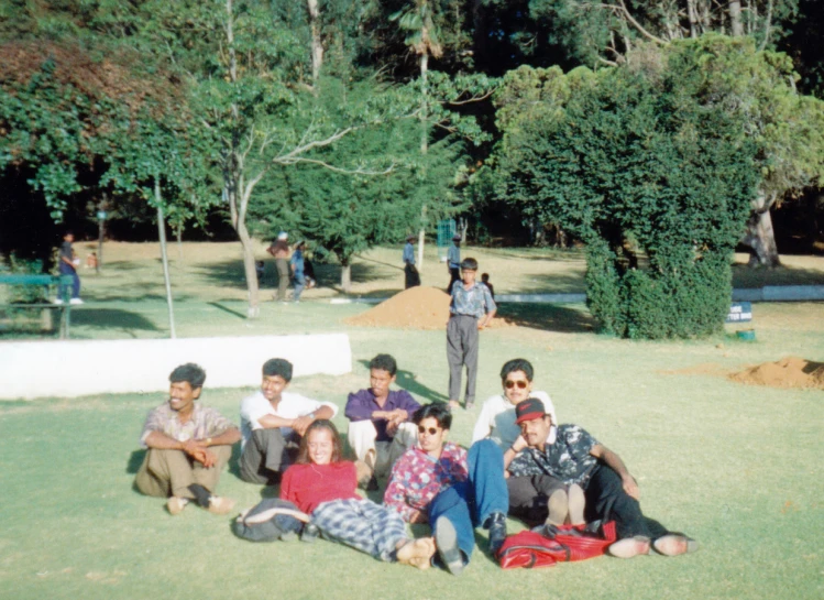 a group of people sitting in the grass by some bushes