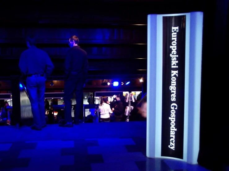 people stand at the entrance of an indoor venue with dark lighting and checkered floor