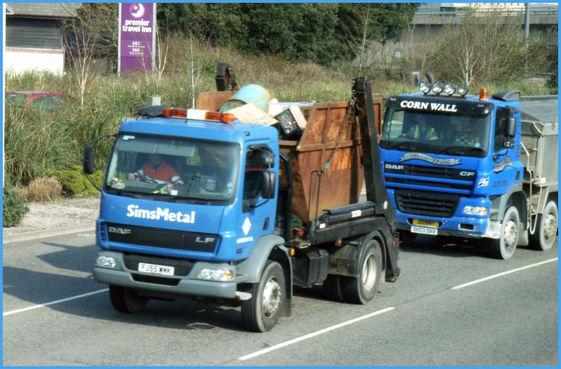 two blue trucks on road next to trees