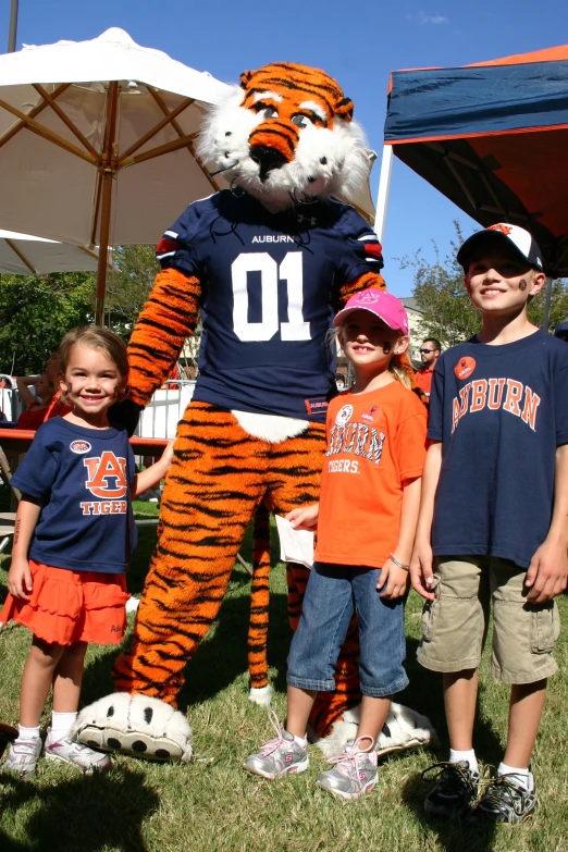 a group of children are standing next to a giant tiger mascot