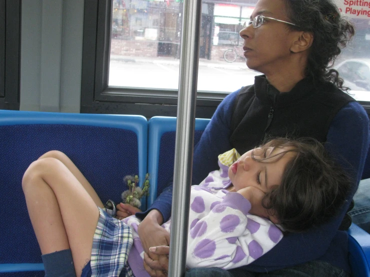 two children sitting on a bus, one sleeping, another holding the child's face as they look out the window