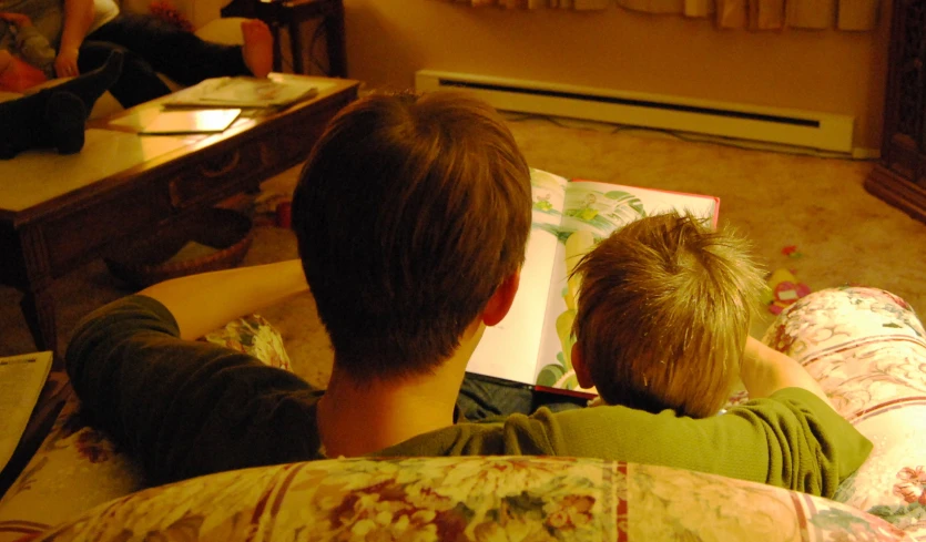 two boys sitting next to each other on the couch with books