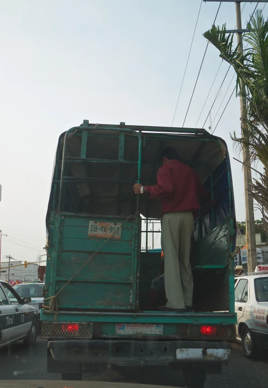 an old man stands on the back of a truck in traffic