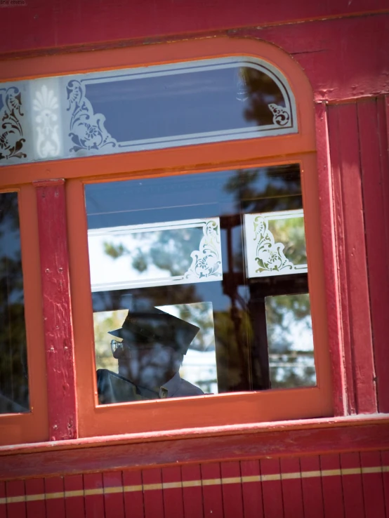 man in hat looking out the window of red train