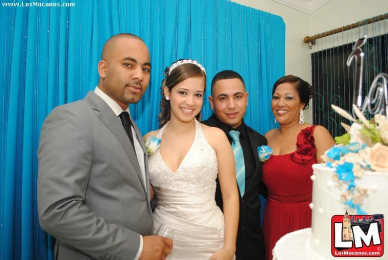 four young people standing around a white cake
