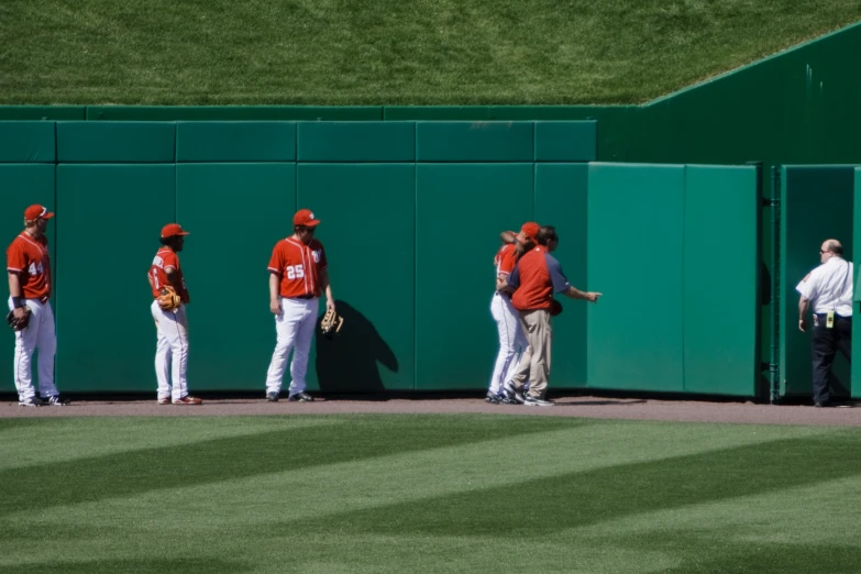 a group of baseball players standing together next to a green wall