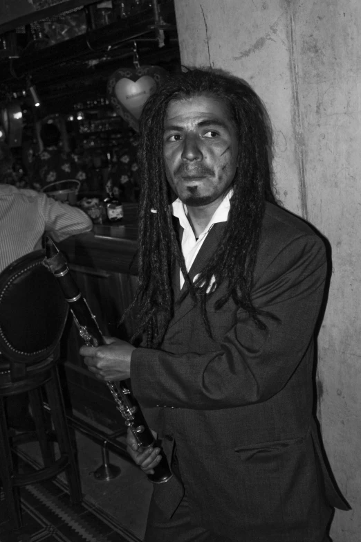 man with dreadlocks holding a glass next to bar