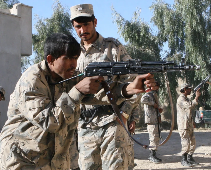 men in uniforms hold up a rifle that is being used