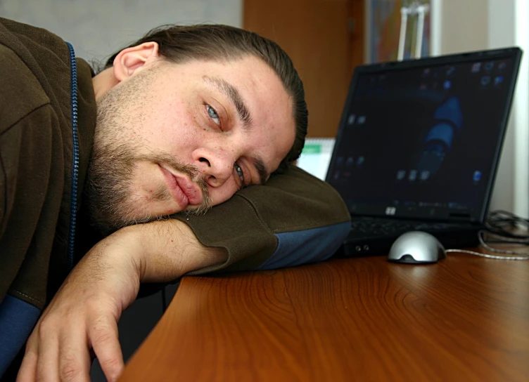 the man with the beard smiles while laying his head on the desk