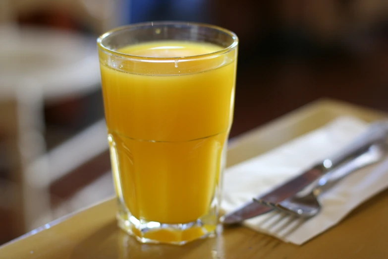 a glass of orange juice on a wooden table with two forks