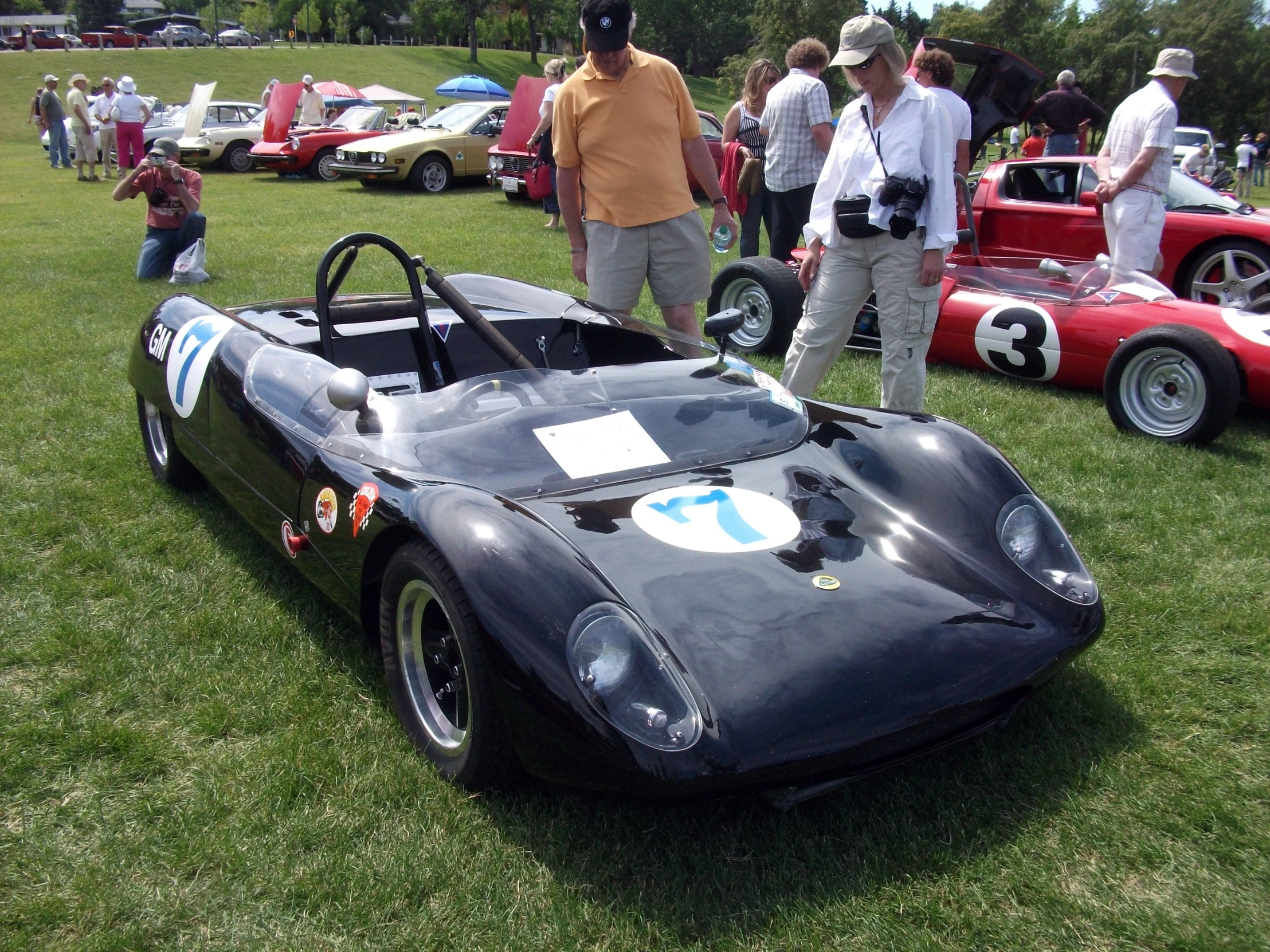 several people standing around a race car in grass