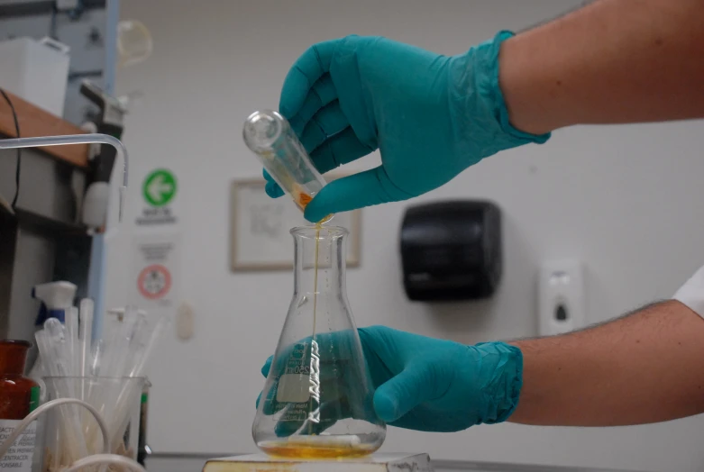 a person in gloves and rubber gloves preparing a beakle with a liquid