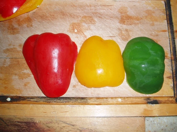 four bell peppers are on a wooden  board
