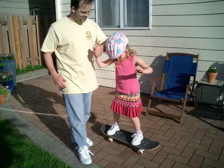 little girl with pink hat riding skateboard with man in yellow shirt