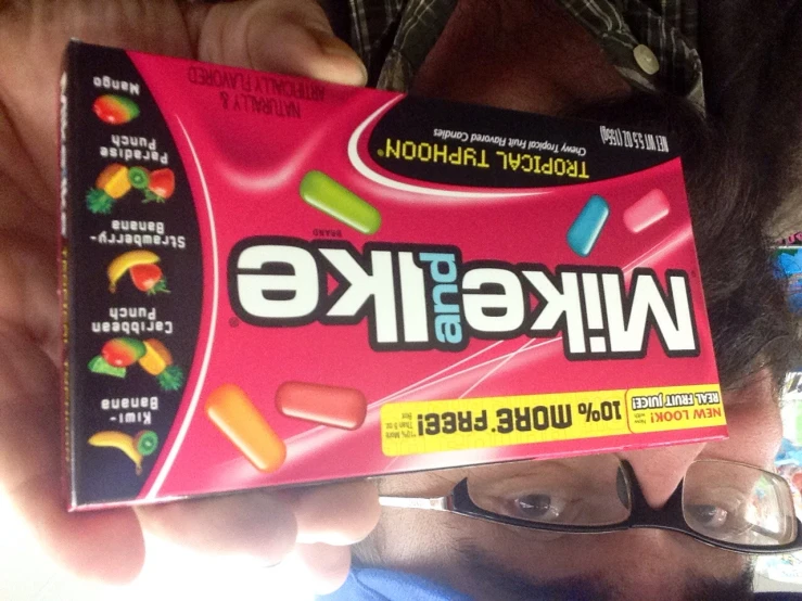 man in glasses holding up a box of mike and ike tropical flavor gums