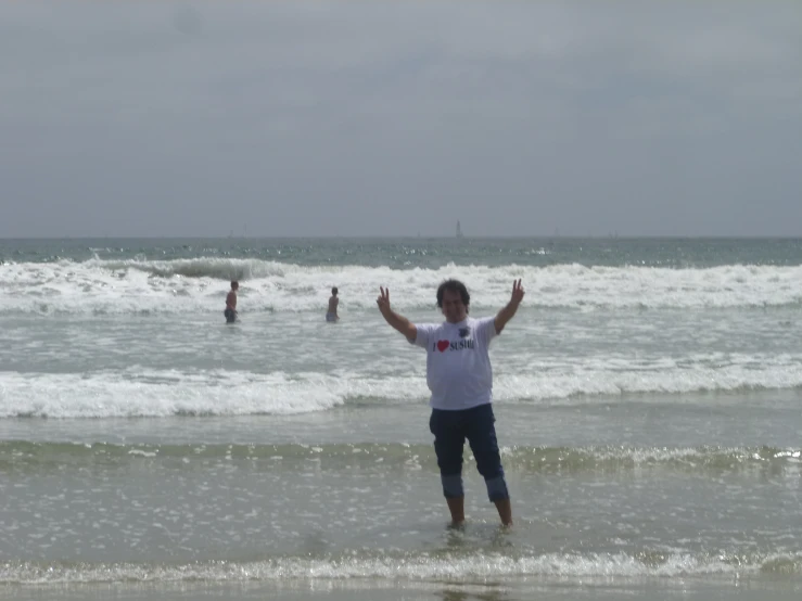 man standing in ocean waves holding up hands