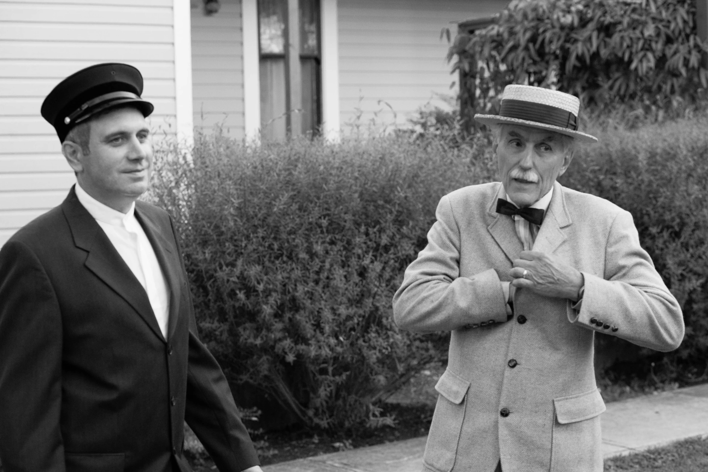 two men in suits are standing in front of some bushes