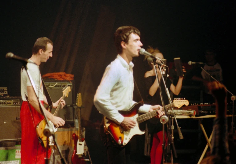 two men standing next to each other while playing guitars