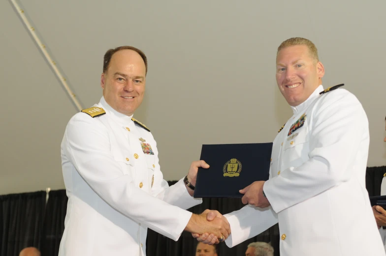 two men in naval uniforms shaking hands with each other
