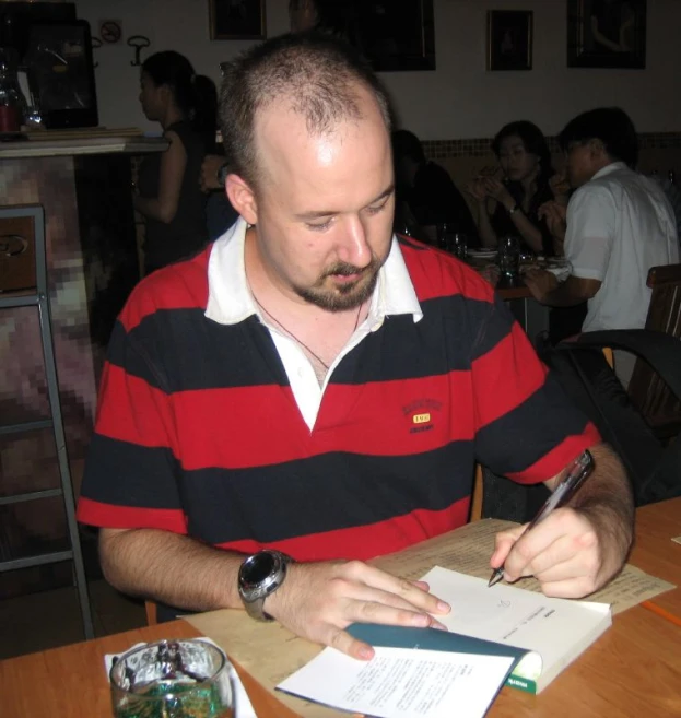 man sitting at a table signing in paper and smiling