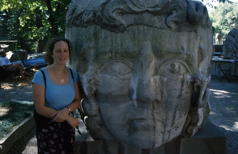 a woman in blue top next to stone head