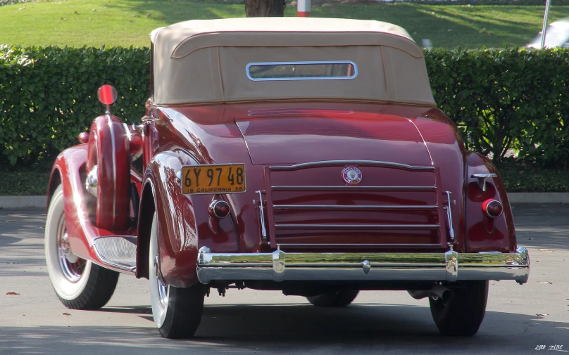 an antique red car parked in front of some hedges