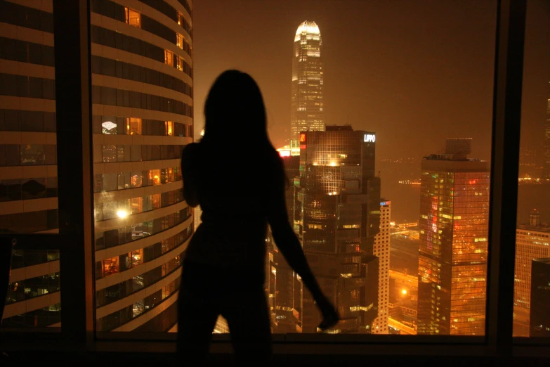 a woman in silhouette against a window overlooking city lights at night