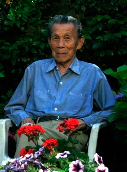 a man with glasses sitting in a chair holding red and purple flowers
