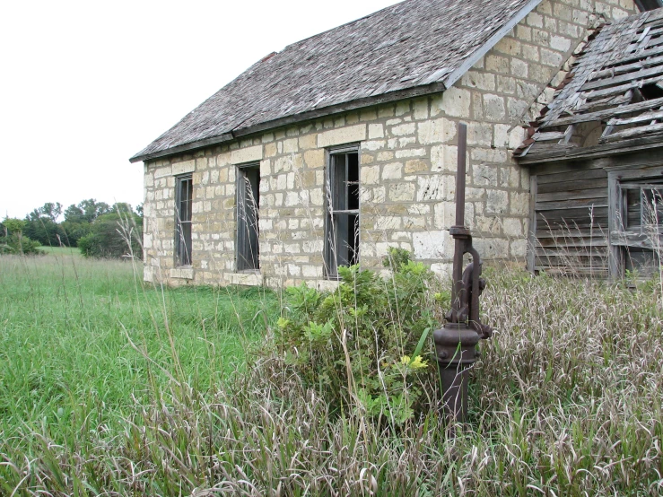 an old brick house with a broken window and door is seen through a grass field