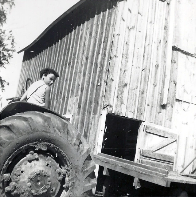 black and white po of boy on tractor near old farm building