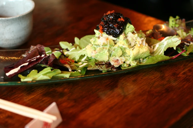 a salad in a plate sitting on a table with chopsticks