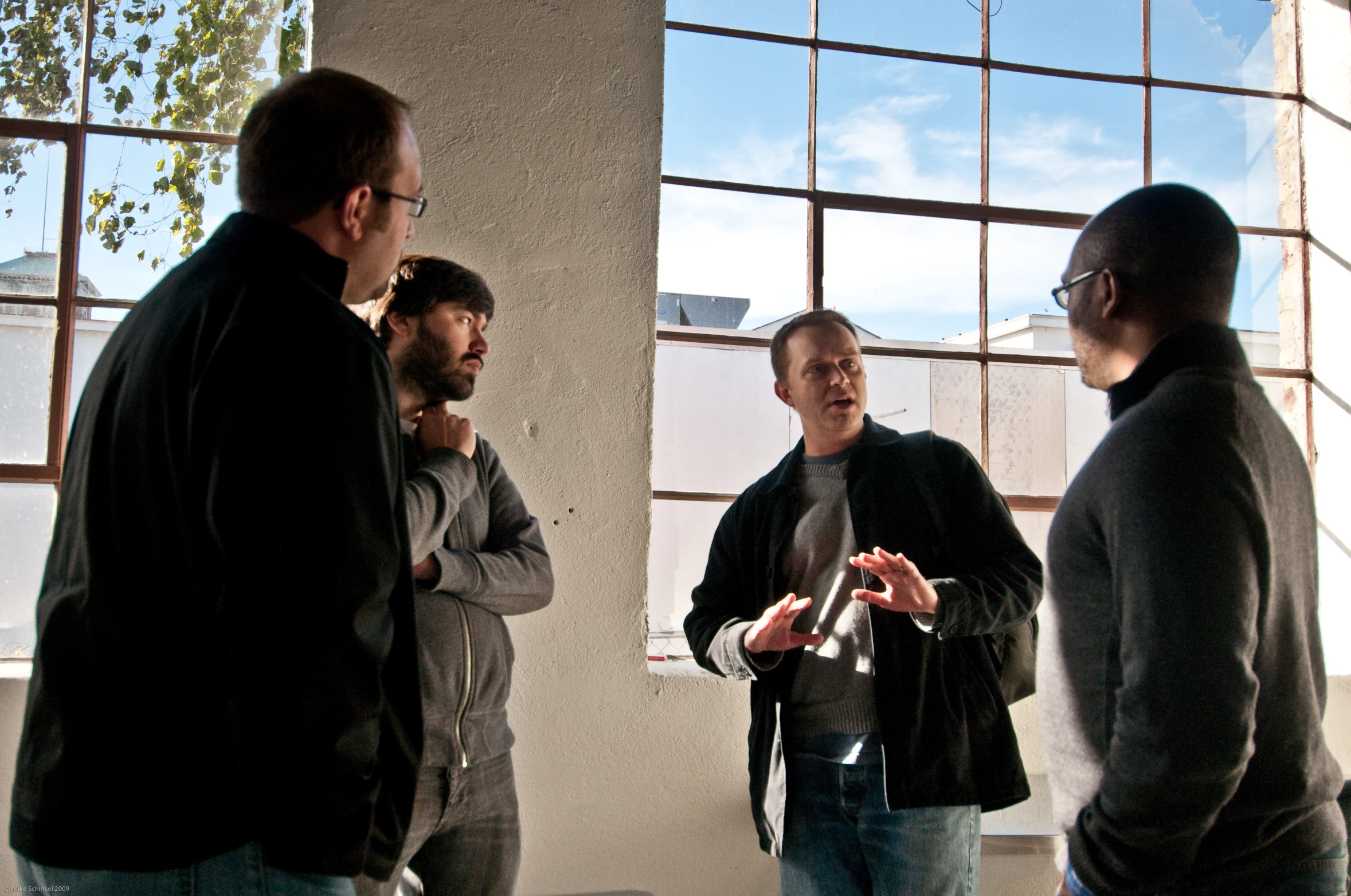 three men standing and talking together with a building in the background