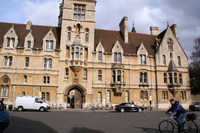 two people riding bicycles past large brick buildings