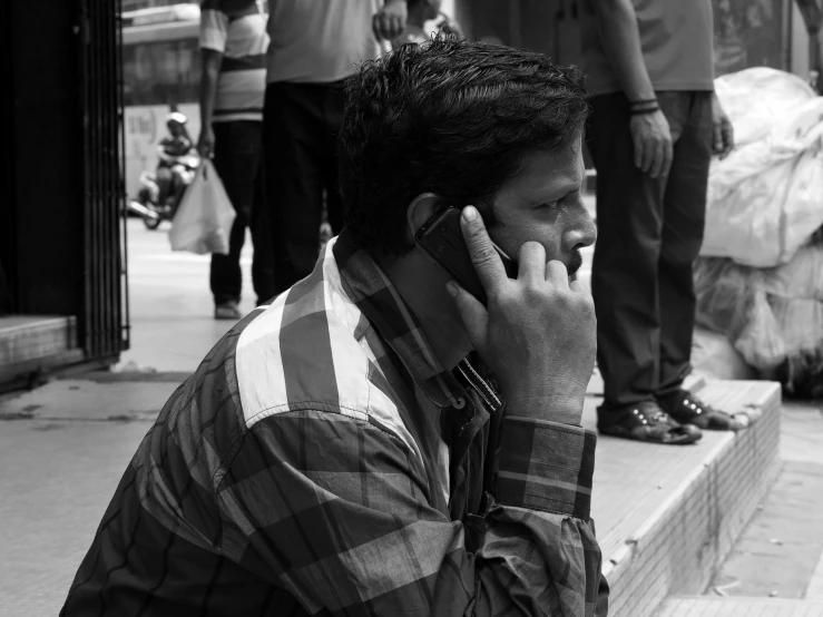 a man talking on his phone on the sidewalk while wearing a checked shirt