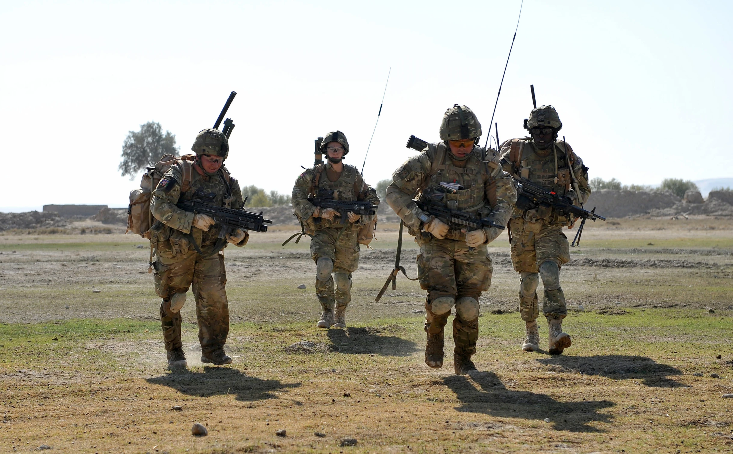 four soldiers in camouflage walking on the grass