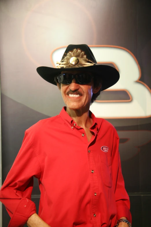 a smiling man wears a hat in front of the logo of racing driver, stewart