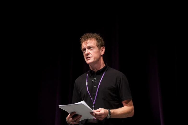 a man stands on stage and holds a sheet of paper