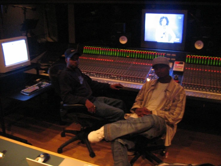 two people sit at a mixing desk with music mixing equipment