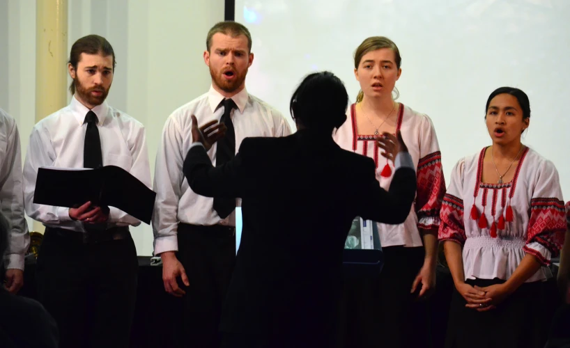 two men and one woman who are standing next to each other with a man in front of them speaking into microphones