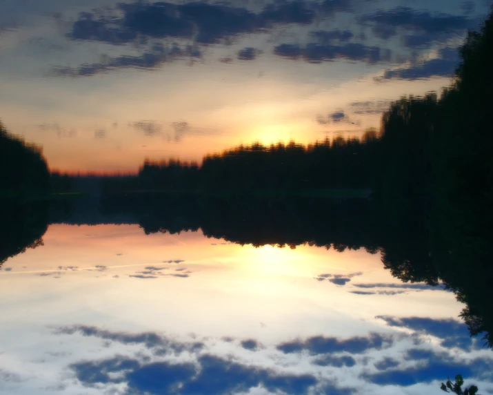 the sun sets behind the clouds over a lake