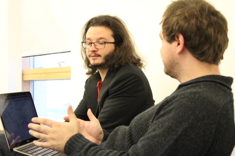 a couple of men sitting in front of a laptop computer