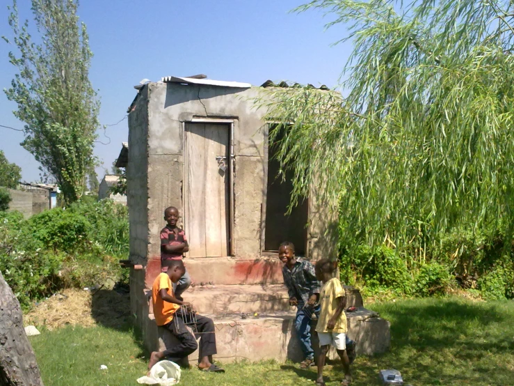 a group of people standing next to a building in a grass field