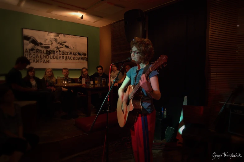 a girl playing a guitar in front of a group of people